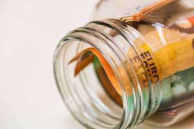 Yatırım yapma ve para tutma kavramı, izole edilmiş olarak yakın plan. Cam bir kavanozda para biriktirme kompozisyonu. Avro banknotlarının ayrıntıları kavanozda.