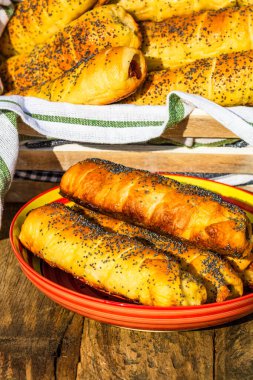 Hamurda pişmiş sosisler tuzlu ve haşhaş tohumları serpiştirilmiş, kırsal bir kompozisyonda. Sosisli börek, lezzetli ev yapımı hamur işleri..