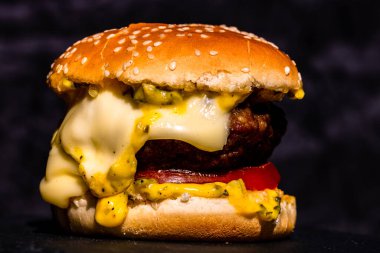Siyah arka planda erimiş peynirli taze sığır etli çizburger.