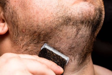 Adam saç makası kullanarak sakalını tıraş ediyor ya da kesiyor.