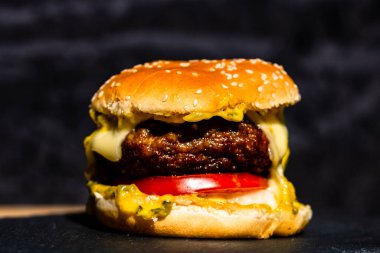 Siyah arka planda erimiş peynirli taze sığır etli çizburger.