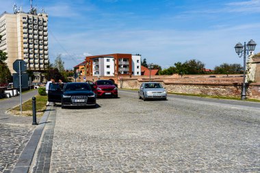 Romanya 'nın Alba Iulia şehrinde kaldırım taşı caddesi boyunca park etmiş arabalar..