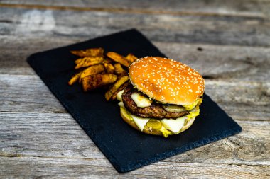 Ev yapımı taze peynirli burger ve ahşap masada kızarmış patates.