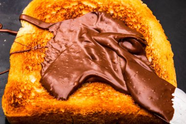 Kızarmış ekmeğe çikolata kreması sürüyorum.