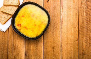 Bir kase çorba ve ahşap masada ekmek.