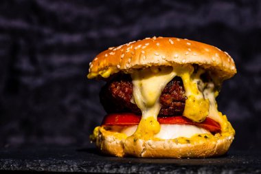 Siyah arka planda erimiş peynirli taze sığır etli çizburger.