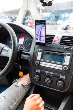 Araba gösterge panelindeki akıllı telefondaki waze haritaları uygulamasını kullanan sürücü yağmurlu bir akşamda şehrin trafiğinde doğru yolu göstermek için harita uygulaması kullanıyor. Bükreş, Romanya, 2020.