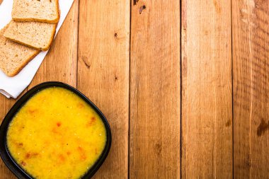 Bir kase çorba ve ahşap masada ekmek.