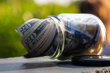 Cam kavanozda para biriktirmek için Amerikan Doları. Tüketim ve ekonomi. İş, bahşiş, finans, tasarruf, bankacılık ve insan kavramı