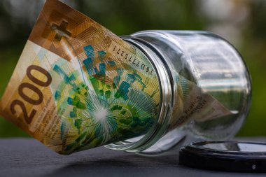 İsviçre frangı CHF banknotu cam kavanozda para biriktiriyor. Tüketim ve ekonomi. İş, bahşiş, finans, tasarruf, bankacılık ve insan kavramı