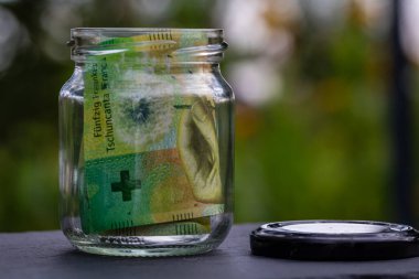 İsviçre frangı CHF banknotu cam kavanozda para biriktiriyor. Tüketim ve ekonomi. İş, bahşiş, finans, tasarruf, bankacılık ve insan kavramı