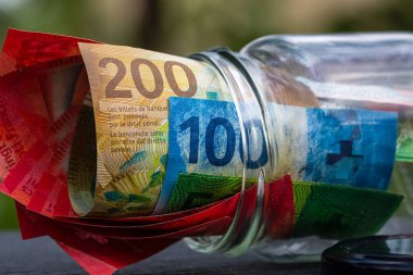 İsviçre frangı CHF banknotu cam kavanozda para biriktiriyor. Tüketim ve ekonomi. İş, bahşiş, finans, tasarruf, bankacılık ve insan kavramı