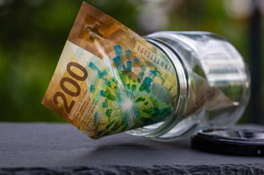 İsviçre frangı CHF banknotu cam kavanozda para biriktiriyor. Tüketim ve ekonomi. İş, bahşiş, finans, tasarruf, bankacılık ve insan kavramı