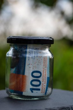 İsviçre frangı CHF banknotu cam kavanozda para biriktiriyor. Tüketim ve ekonomi. İş, bahşiş, finans, tasarruf, bankacılık ve insan kavramı