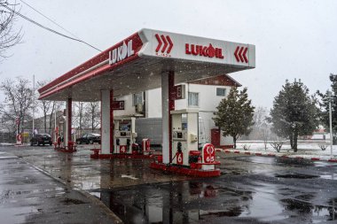 LUKOIL benzin istasyonunun dışı. Benzin pompaları ve arabalar kar yağarken yakıt ikmali yapıyorlar.