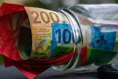 İsviçre frangı CHF banknotu cam kavanozda para biriktiriyor. Tüketim ve ekonomi. İş, bahşiş, finans, tasarruf, bankacılık ve insan kavramı