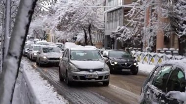 Bükreş 'te kar fırtınası ve yoğun kar yağışı var. Trafikte arabalar ve insanlar karlı yollarda yürüyor.
