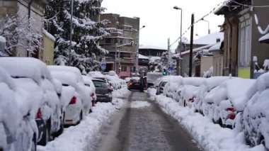 Bükreş 'te kar fırtınası ve yoğun kar yağışı var. Trafikte arabalar ve insanlar karlı yollarda yürüyor.