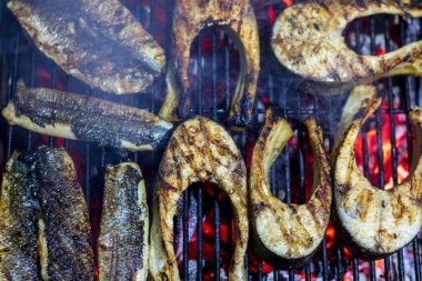 Sıcak ızgarada pişen taze balık filetoları. Sağlıklı açık hava pikniği için duman ve ateş alevleri.