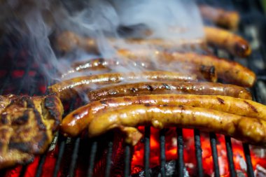 Domuz bifteği ve sosis sıcak ızgarada pişiyor. Açık hava pikniği için duman ve alevlerle.