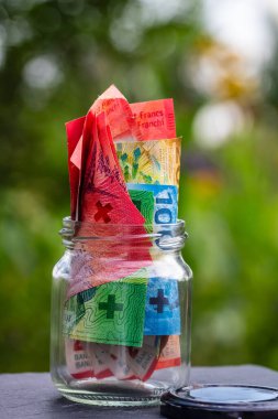 İsviçre frangı CHF banknotu cam kavanozda para biriktiriyor. Tüketim ve ekonomi. İş, bahşiş, finans, tasarruf, bankacılık ve insan kavramı