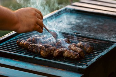 Ateşli ve dumanlı barbekü ızgarasında mici veya mititei adı verilen geleneksel Romen köftelerini hazırlamak