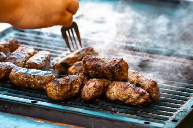 Ateşli ve dumanlı barbekü ızgarasında mici veya mititei adı verilen geleneksel Romen köftelerini hazırlamak
