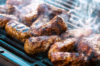 Ateşli ve dumanlı barbekü ızgarasında mici veya mititei adı verilen geleneksel Romen köftelerini hazırlamak