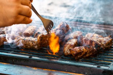 Ateşli ve dumanlı barbekü ızgarasında mici veya mititei adı verilen geleneksel Romen köftelerini hazırlamak