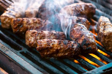 Ateşli ve dumanlı barbekü ızgarasında mici veya mititei adı verilen geleneksel Romen köftelerini hazırlamak