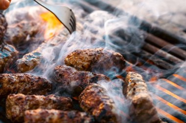 Ateşli ve dumanlı barbekü ızgarasında mici veya mititei adı verilen geleneksel Romen köftelerini hazırlamak