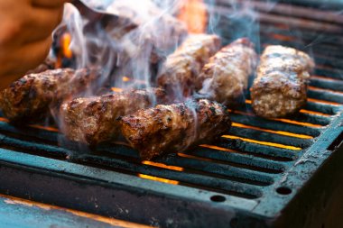 Ateşli ve dumanlı barbekü ızgarasında mici veya mititei adı verilen geleneksel Romen köftelerini hazırlamak