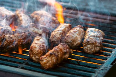Ateşli ve dumanlı barbekü ızgarasında mici veya mititei adı verilen geleneksel Romen köftelerini hazırlamak