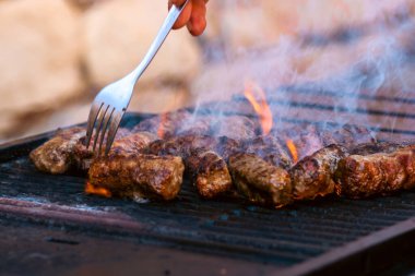 Ateşli ve dumanlı barbekü ızgarasında mici veya mititei adı verilen geleneksel Romen köftelerini hazırlamak