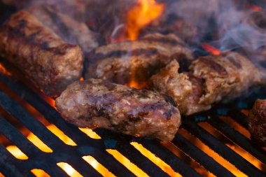 Ateşli ve dumanlı barbekü ızgarasında mici veya mititei adı verilen geleneksel Romen köftelerini hazırlamak