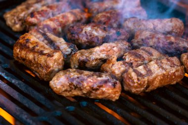 Ateşli ve dumanlı barbekü ızgarasında mici veya mititei adı verilen geleneksel Romen köftelerini hazırlamak