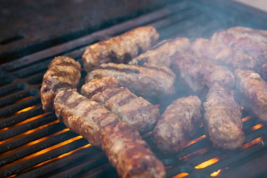 Ateşli ve dumanlı barbekü ızgarasında mici veya mititei adı verilen geleneksel Romen köftelerini hazırlamak