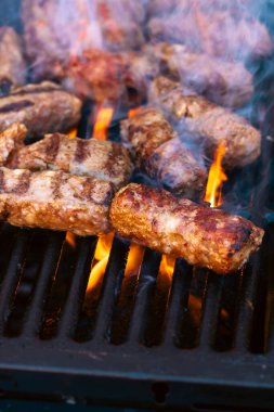 Ateşli ve dumanlı barbekü ızgarasında mici veya mititei adı verilen geleneksel Romen köftelerini hazırlamak
