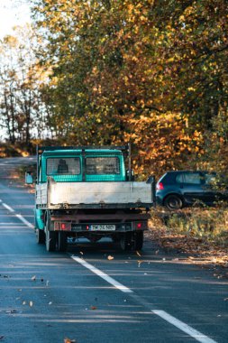 Boş bir asfalt yolda giden araba altın sonbahar manzaralı bir ormanın içinden geçiyor.