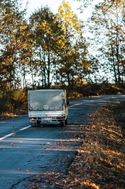 Boş bir asfalt yolda giden araba altın sonbahar manzaralı bir ormanın içinden geçiyor.