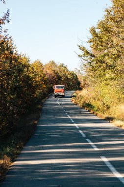 Boş bir asfalt yolda giden araba altın sonbahar manzaralı bir ormanın içinden geçiyor.