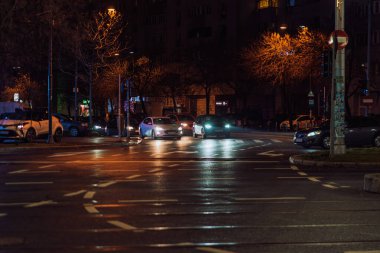 Gece Bükreş 'teki şehir sokak sahnesinde otomobil ışıkları ve boş şehir yolları yer alıyor