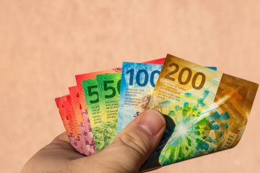 İsviçre frangı para banknotlarını tutan adam, İsviçre CHF para biriminin kağıt dokusu ve sembollerini gösteriyor