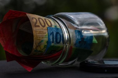 İsviçre frangı CHF banknotu cam kavanozda para biriktiriyor. Tüketim ve ekonomi. İş, bahşiş, finans, tasarruf, bankacılık ve insan kavramı