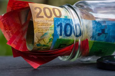 İsviçre frangı CHF banknotu cam kavanozda para biriktiriyor. Tüketim ve ekonomi. İş, bahşiş, finans, tasarruf, bankacılık ve insan kavramı