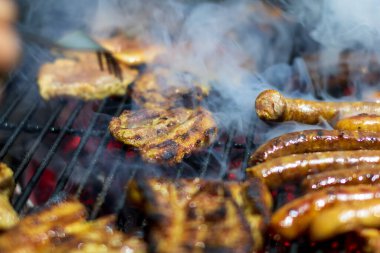 Domuz bifteği ve sosis sıcak ızgarada pişiyor. Açık hava pikniği için duman ve alevlerle.
