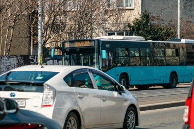 Bükreş 'te güneşli bir bahar gününde yoğun bir şehir caddesinde trafik ve trafik sıkışıklığında bekleyen banliyö araçları görülüyor