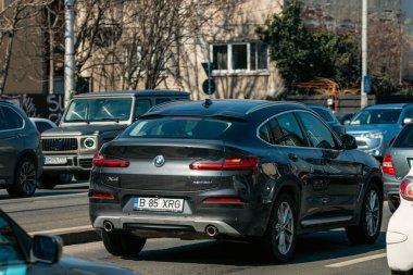 Bükreş 'te güneşli bir bahar gününde yoğun bir şehir caddesinde trafik ve trafik sıkışıklığında bekleyen banliyö araçları görülüyor