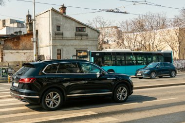 Bükreş 'te güneşli bir bahar gününde yoğun bir şehir caddesinde trafik ve trafik sıkışıklığında bekleyen banliyö araçları görülüyor