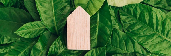 Banner con casa de madera en miniatura sobre hojas verdes. Concepto de casa respetuoso del medio ambiente y eficiente energéticamente. — Foto de Stock